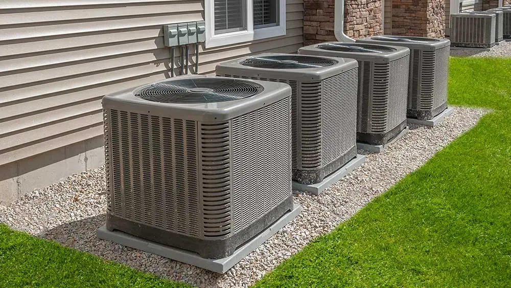 Row of outdoor condensers on pads along a house