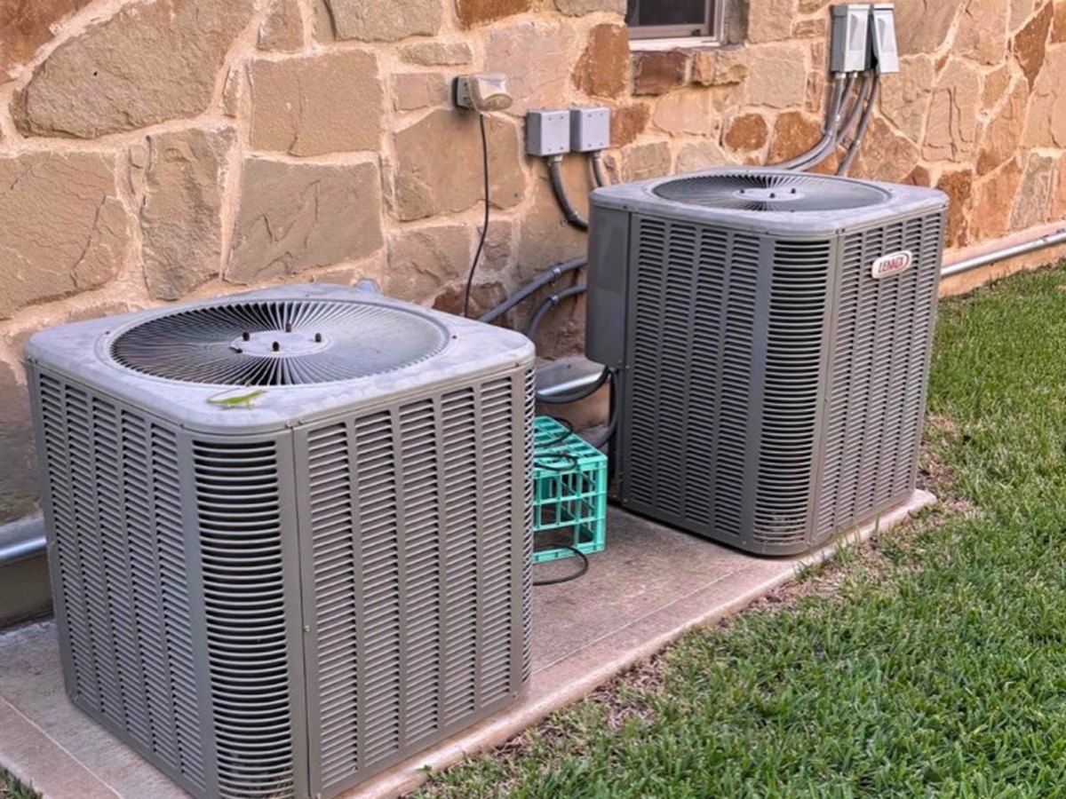 Two new condensers set on a shared pad after a double system changeout at a Central Texas stone home
