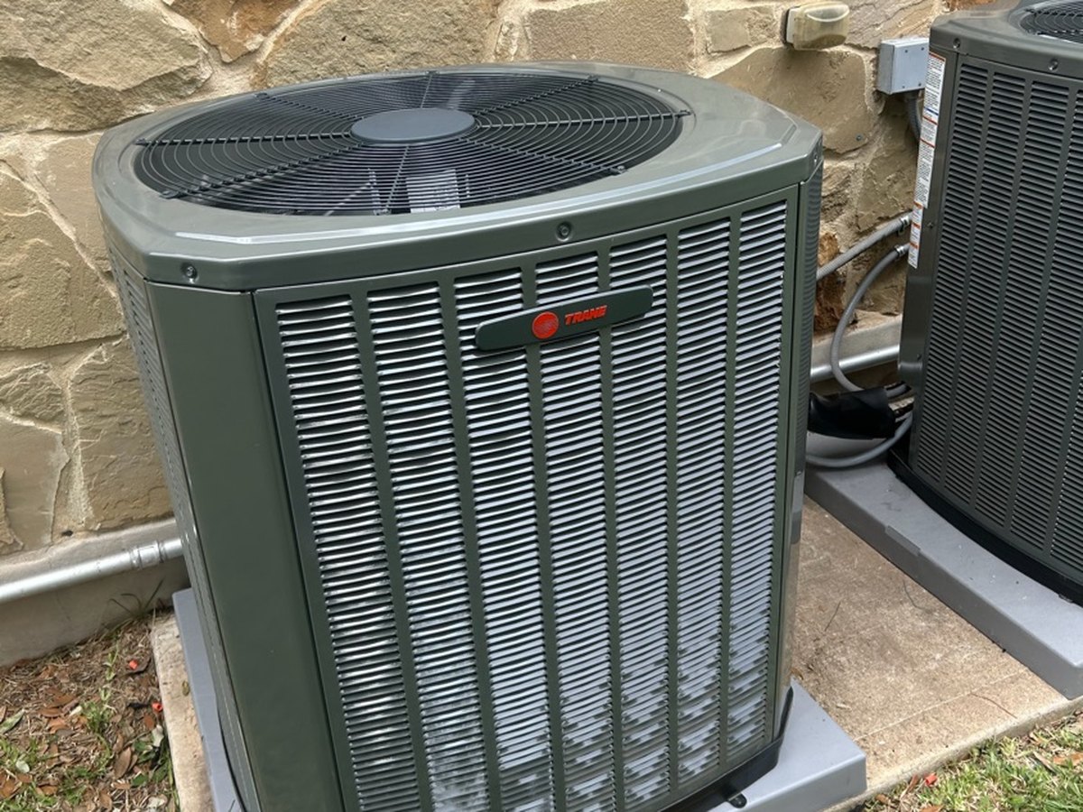 New Trane condenser set on a pad against a flagstone wall in Austin, TX